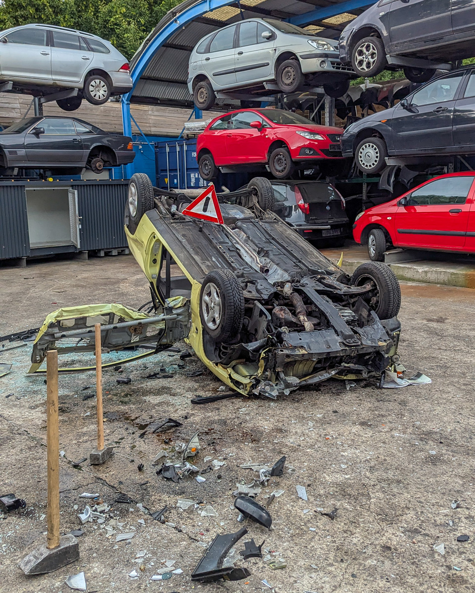 Ein demoliertes Auto mi Warndreieck auf einem Schrottplatz