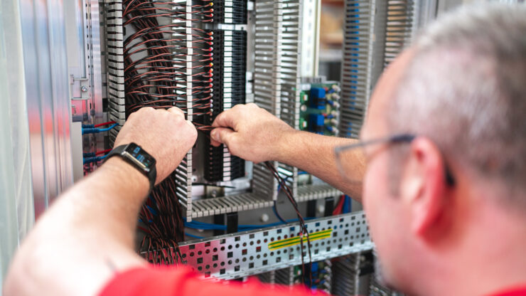 Blick über die Schulter eines Mannes, der an der Verkabelung in einem Schaltschrank arbeitet