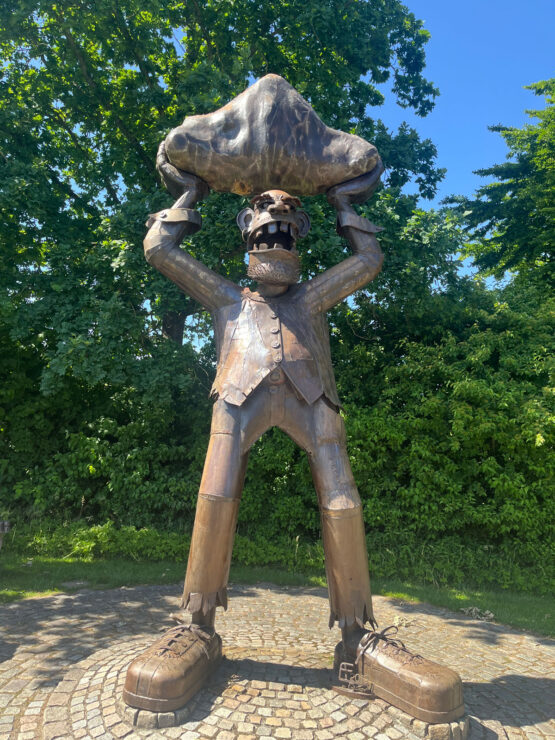 Eine übergroße Skulptur eines stilisierten Menschen, der einen großen Felsen über den Kopf hebt