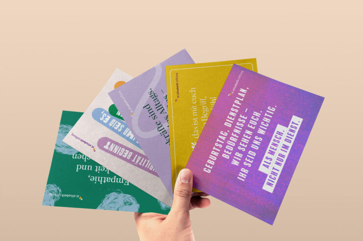 Eine Hand hält vier verschieden gestaltete Postkarten von der St. Elisabeth Stiftung in einem Fächer