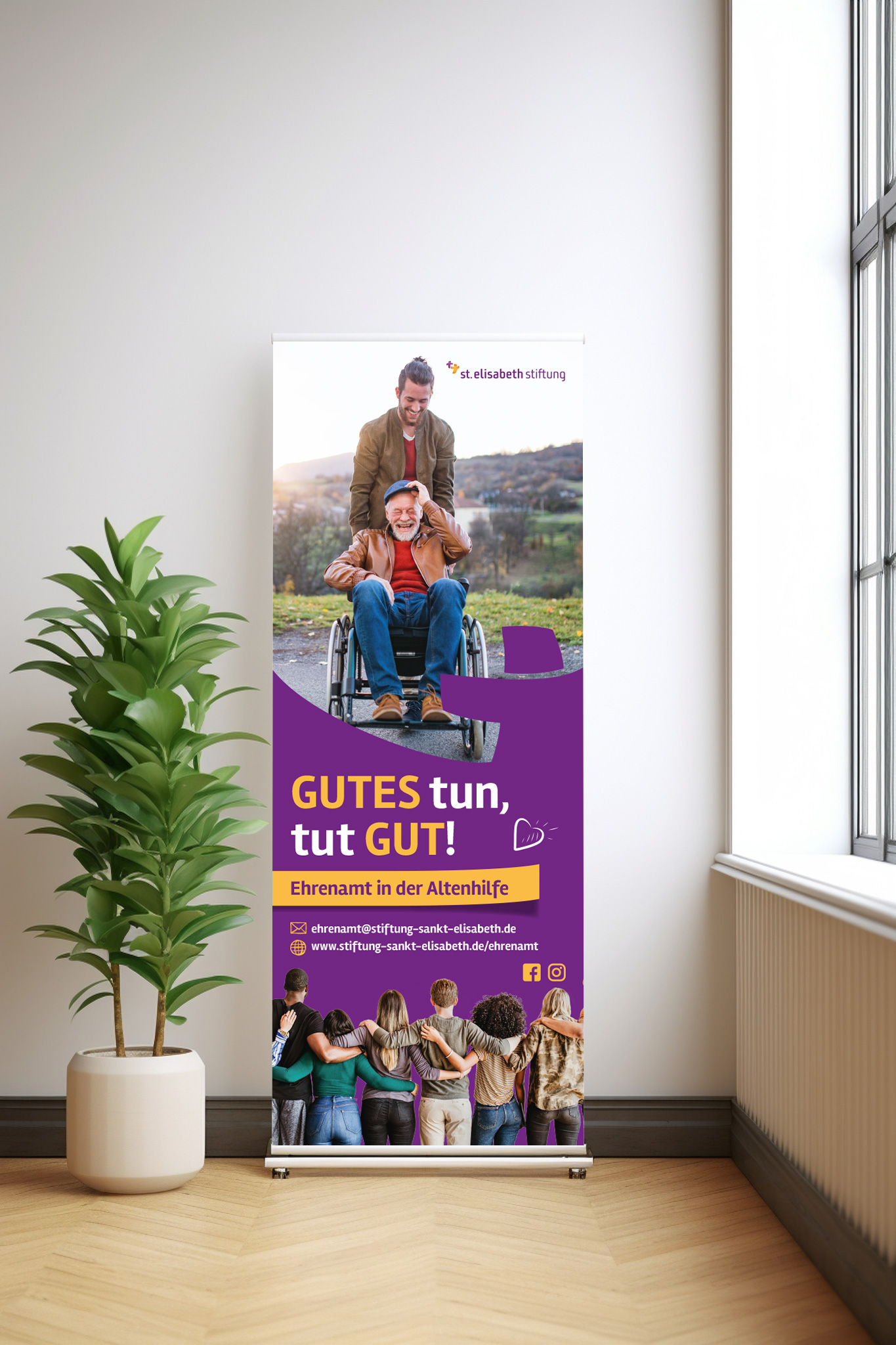 Ein Roll-Up Banner von der St. Elisabeth Stiftung steht neben einer grünen Topfpflanze in einem hellen Raum